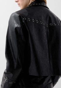 Sort læderjakke med en cropped design, tekstureret overflade og sølvfarvede nitter langs ryggen og ærmerne.