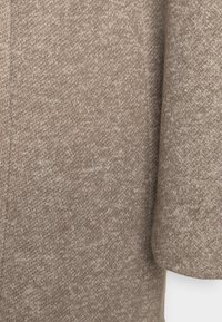 Knitted sweater in light brown with a soft, textured surface. Features a subtle mixed pattern and loose sleeves. No visible fasteners.