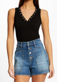 Body nero a coste senza maniche con scollatura a V, dettagliato con borchie argentate; abbinato a pantaloni shorts in denim a vita alta con chiusura a bottone.