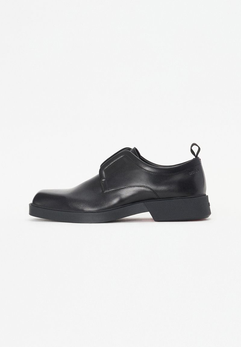 Chaussure en cuir noir à enfiler avec bout rond, talon bas, col matelassé et languette arrière sur fond blanc.