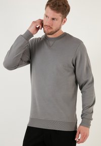Felpa di cotone grigia con scollo rotondo, maniche lunghe, polsini a coste e un motivo testurizzato. Presenta un orlo dritto e accenti minimi.