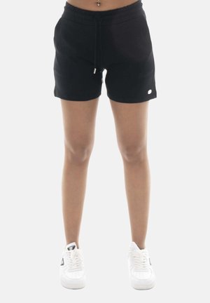 Femme portant un short noir à cordon et des baskets blanches, montrant ses jambes et son ventre avec un piercing au nombril.