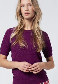 Suéter violeta de manga corta con un patrón de diamante texturizado, cuello y dobladillo acanelados, que presenta un estilo ajustado y un acabado suave.