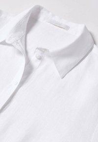 Chemise en lin blanc à manches longues avec un col pointu et deux boutons visibles sur la patte de boutonnage avant.