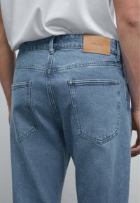 Modré džínové kalhoty s vintage umytím, s koženým štítkem označeným "Massimo Dutti" a dvěma zadními kapsami.