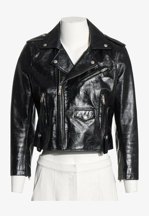 Chaqueta negra de cuero recortada de motorista con cremalleras plateadas, botones automáticos y cuello con solapa ancha sobre un torso de maniquí blanco.