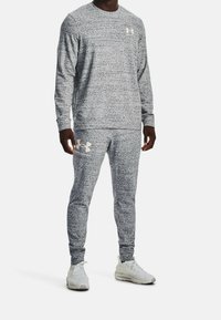 Sudadera y pantalones deportivos grises hechos de una tela texturizada, con un patrón sutil y el logo dorado de Under Armour en el pecho y el muslo.