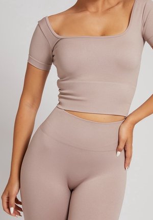 Mujer con conjunto a juego de crop top beige acanalado y leggings de cintura alta sobre un fondo claro.