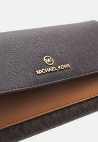 Portafoglio Michael Kors in tessuto nero e marrone con emblema dorato sulla chiusura a pattina.
