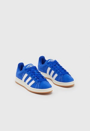 Paire de baskets Adidas Campus bleues avec des bandes blanches et des semelles en gomme sur un fond gris clair.