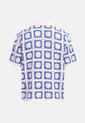 Camisa de punto de manga corta con patrones de cuadrados de crochet en azul y blanco, que presenta una textura de tejido abierto y un cuello.