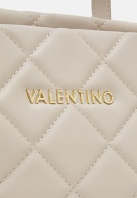 Vadderad beige konstläderhandväska med guldigt "VALENTINO"-logotyp. Har diamantmönster i sömnaden och en mjuk textur.