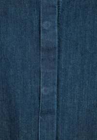 Tissu en denim bleu foncé avec une texture lisse et des motifs de tissage visibles, comportant une couture centrale et de subtiles variations de couleur.