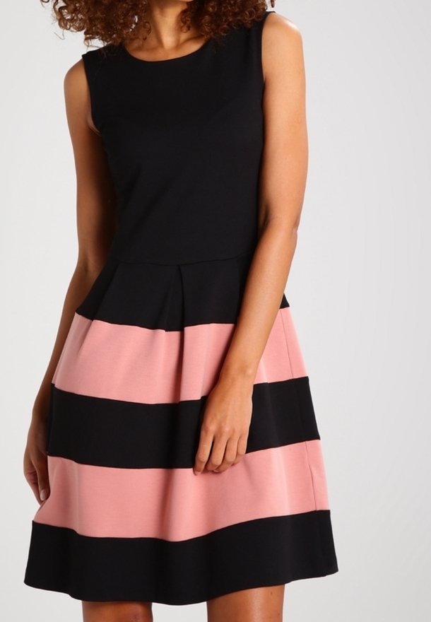 Femme portant une robe sans manches avec un haut noir et des larges rayures horizontales roses et noires alternées sur la jupe.