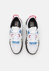Baskets Versace Jeans Couture blanches, noires, rouges et bleues avec lacets et sangles brandées sur fond blanc.