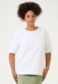 T-shirt en coton blanc à manches courtes, col rond, coupe décontractée, avec une texture lisse et des fentes sur les côtés pour plus de confort.