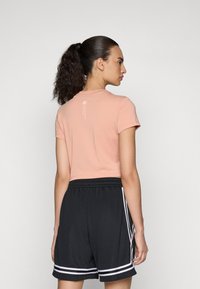 Lys rosa crop t-skjorte med korte ermer, med en subtil logo på baksiden. Kombinert med sorte shorts med hvite sidedetaljer.