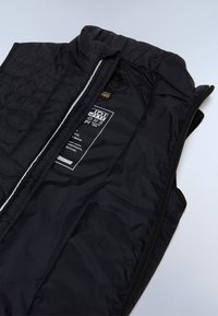 Černá prošívaná vesta s vysokým límcem a zapínáním na zip, s hladkou, lehkou vnitřní látkou a vnitřním označením péče.