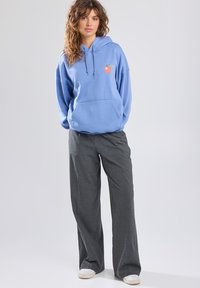 Light blue hoodie with a front pocket and orange fruit graphic; paired with gray wide-leg pants and white shoes. Soft texture, casual fit.