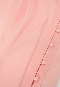 Közelkép puha rózsaszín anyagról, díszes anyaggal bevont gombokkal és finom, rétegezett részletekkel az öltözéken.