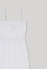 Bílý overal bez ramínek s elastickým pasem, zdobený vyšíváním a bočními kapsami. Lehce materiál s hladkou strukturou.