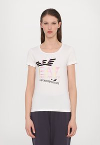 Bílá tričko s krátkými rukávy a kulatým výstřihem, které na přední straně zdobí vícebarevný grafický logotyp značky Emporio Armani.