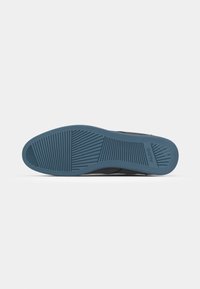 Sorte slip-on sko med en blå gummisåle. Sålen har et teksturert mønster for grep og friksjon.