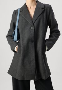 Grå kappa i ullblandning med en figursydd design, slagkrage, två framfickor och svarta knappar. Matchad med en blå handväska.