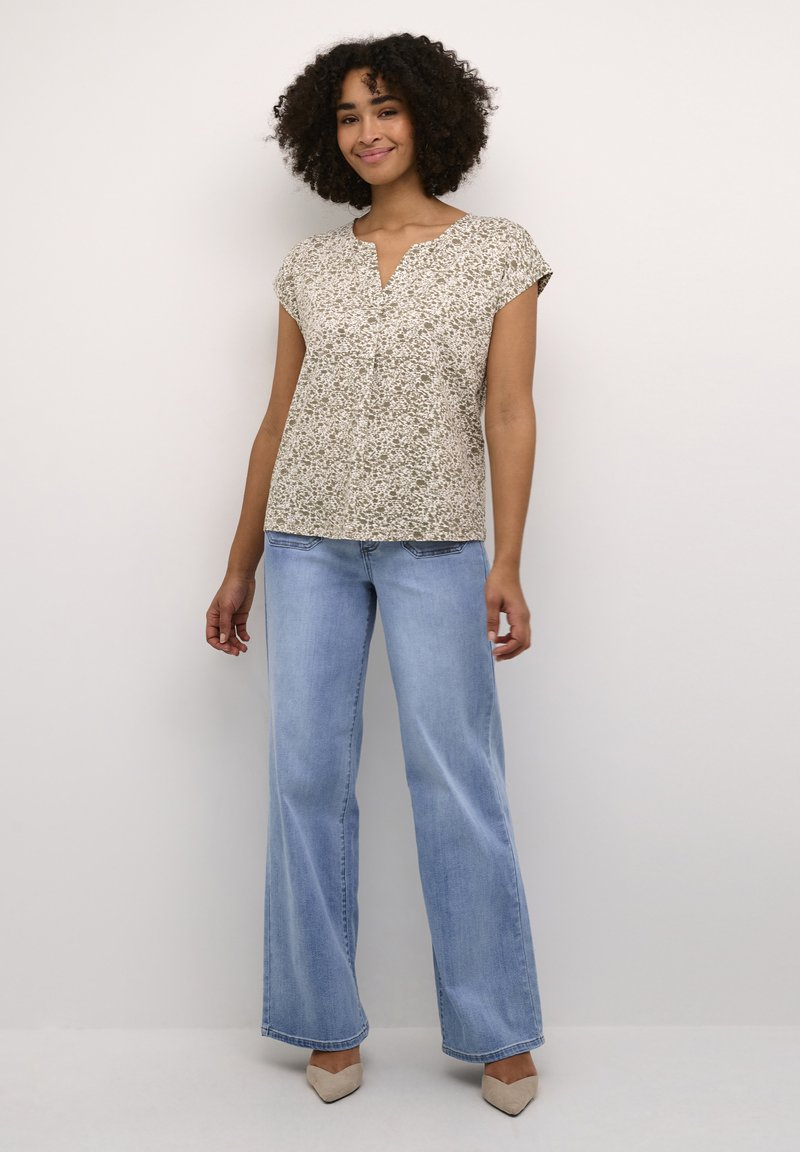 Haut à manches courtes à motifs floraux dans des tons crème et vert. Présente un col en goutte d'eau. Assorti avec un jean bleu clair évasé et des talons beiges.