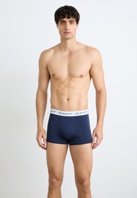Marineblaue Boxershorts aus weicher Baumwolle, mit einem weißen elastischen Bund, der mit wiederholtem Branding versehen ist. Glatte Textur und taillierte Passform.