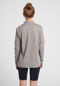Pullover grigio a maniche lunghe con un motivo a trama e colletto alto, abbinato a pantaloni corti neri aderenti.
