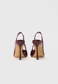 Burgunderfargede patentlæder højhælede sko med slingback-design og spidse tåer, der har en tynd stiletto-hæl og beige inderside.