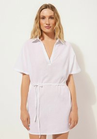 Vestido de lino blanco con cuello, mangas cortas y escote en V. Presenta un cinturón con cordón en la cintura y un corte relajado.