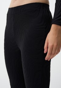 Zwarte legging met een textuur golfpatroon, hoge tailleband en een aansluitend ontwerp, gemaakt van een rekbare, gladde stof.