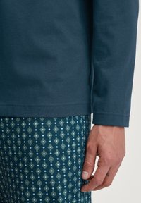 Chemise à manches longues bleu foncé avec une texture lisse, associée à un pantalon vert et bleu à motifs, arborant un motif en losange.