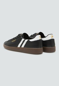 Czarne skórzane sneakersy z białymi paskami i teksturowaną brązową podeszwą. Posiadają złote logo oraz wyściółkę w kołnierzu dla komfortu.