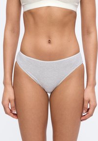 Žena oblečená v svetlosivých bavlnených nohavičkách typu bikini a bielom podprsenke, zobrazená od polovice brucha po polovicu stehien na jednoduchom pozadí.