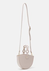 Beige leather handbag with a semi-circular shape, circular cutout handle, and gold hardware. Adjustable strap for versatility.