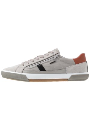Sneaker beige basso con chiusura frontale a lacci, cerniera laterale, dettaglio a striscia nera, suola bianca, punta grigia strutturata e dettaglio marrone sul tallone.
