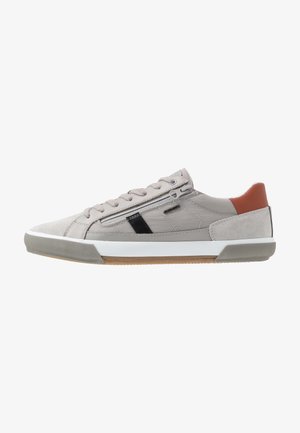 Sneaker beige basso con chiusura frontale a lacci, cerniera laterale, dettaglio a striscia nera, suola bianca, punta grigia strutturata e dettaglio marrone sul tallone.