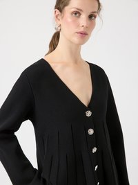 Black long-sleeve cardigan with a deep V-neck, featuring pleated texture and silver floral buttons along the front. Smooth, knit fabric.