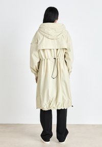 Világos bézs színű kapucnis dzseki, rugalmas derékkal, ráncolt aljjal és széles ujjakkal. Sima textúra, hátoldalán réteges kialakítással.