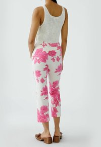 Débardeur en maille blanc associé à un pantalon court à motif floral rose. Le pantalon a une coupe droite et des poches latérales. Sandales à talons carrés marron.