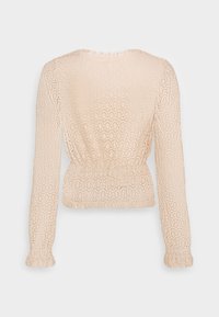 Beige Spitzenbluse mit langen Ärmeln, die ein ovales Muster, einen gerafften Bund und Rüschensäume für Textur und Detail aufweist.