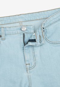 Vaqueros de mezclilla azul claro con cremallera parcialmente bajada y botón metálico etiquetado "Dan John Denim".