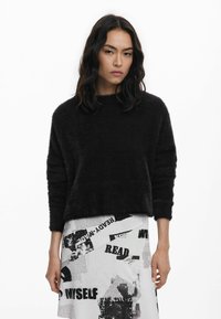 Schwarzer, flauschiger Pullover mit Rundhalsausschnitt und lockerer Passform; lange, leicht gepuffte Ärmel; kombiniert mit einem grafischen, gemusterten Rock.