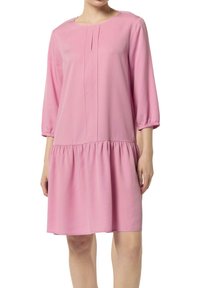 Rosa, knielanges Kleid aus leichtem Stoff. Es hat einen runden Ausschnitt, Dreiviertelärmel und einen gerafften, gestuften Saum.