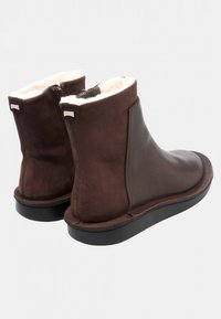 Botas de cuero marrón hasta el tobillo con un suave forro crema, textura lisa, puntera redonda y suela negra; cuentan con un cierre en la parte trasera para poner y quitar fácilmente.
