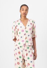 Bloemrijke blouse met korte mouwen in crème stof, voorzien van meerkleurige bloemenpatronen, V-hals en een knoopsluiting aan de voorkant.