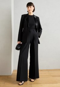 Černý přizpůsobený blazer se saténovými klopami, odpovídající široké kalhoty a fitted černý top. Doplněno malou černou taškou a sandály na řemínky.